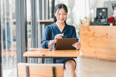 Kafede tablet kullanan, gülümseyen ve eğlenen bir kadın..