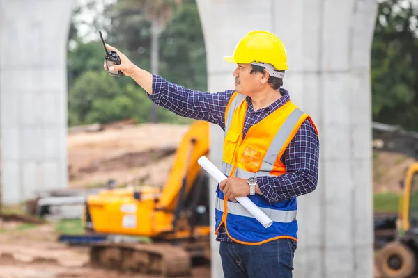 Engineer man in hardhat with Two-Way radio at the infrastructure construction site, Architect with blueprints at a construction site