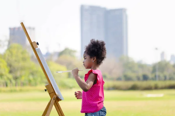 Kid girl painting on canvas in the garden, Happy child girl drawing a picture outdoors