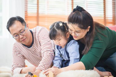 Asyalı aile oturma odasında oynuyor, kız çocuk kız anne ve baba evde oyuncak oynuyorlar.