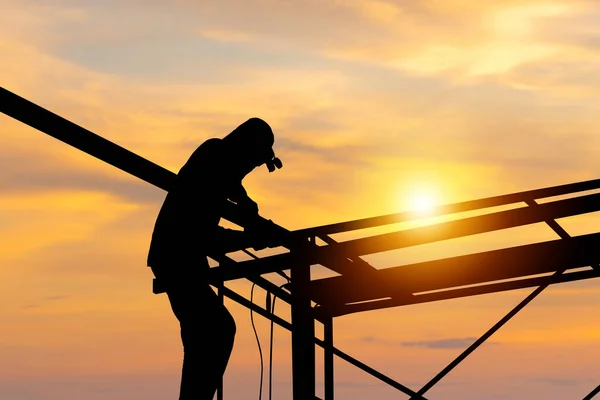 Silhouette of welder worker on building site, construction site at sunset in evening time