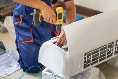 Asyalı teknisyen bir müşterinin evine klima kuruyor, genç bir tamirci havalandırma ünitesini tamir ediyor, onarım ve onarım işleriyle uğraşıyor.