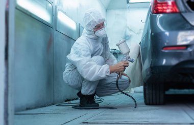 Tamirci odada araba boyuyor. Sprey tabanca ve hava fırçası kullanan ve araba boyayan işçiler, araba tamir ve onarım servislerini boyayan işçiler.