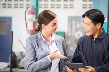 Tamirhanede kadın müdür ve oto tamircisi, tamirci ve genç bayan müşteri birlikte tamirhanede, araba tamiri ve bakım konseptinde konuşuyorlar.
