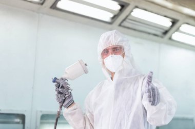 Neşeli işçi, tamirhanede baş parmak gösteriyor, tamirci, sprey tabancayla araba boyuyor, araba tamiri ve bakım servisi yapıyor.