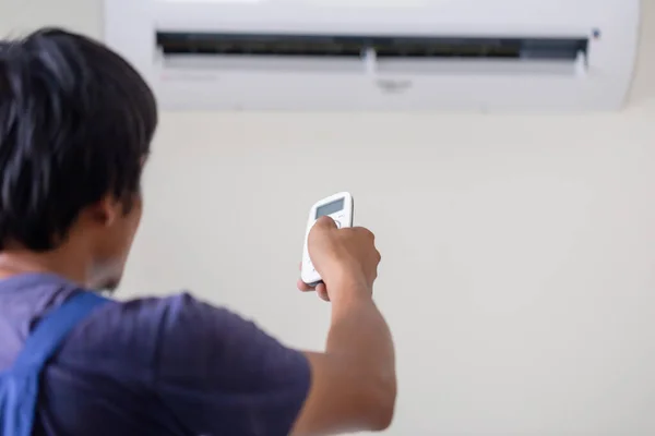 Air conditioner inside the room with technician operating remote controller, Repairman fixing air conditioner unit, Maintenance and repairing concepts