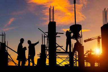 Mühendis ve işçi ekibinin silueti inşaat alanındaki projeyi kontrol ediyor. İnşaat alanı akşam saatlerinde gün batımına kadar arkaplanda.