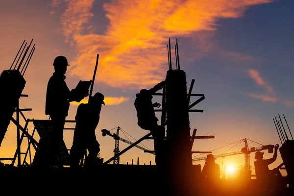 現場の背景でプロジェクトをチェックするエンジニアと労働者のチームのシルエット 夕方の時間の背景で日没と建設現場 — ストック写真