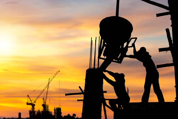 現場の背景でプロジェクトをチェックするエンジニアと労働者のチームのシルエット 夕方の時間の背景で日没と建設現場 — ストック写真