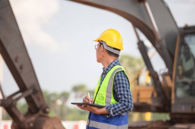 Engineer checking project at the building site, Man in hardhat with digital tablet at infrastructure construction site clipart