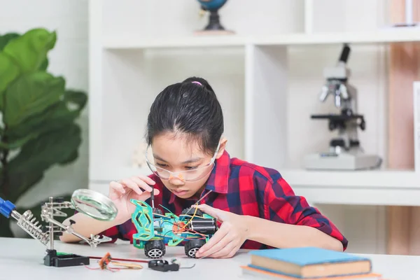 Asian child girl students build robotic cars, kids learn to program robot vehicles