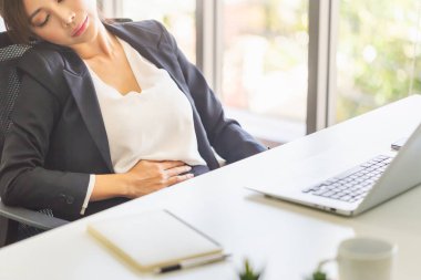 Midesi ağrıyan bir kadın ofiste kendini iyi hissetmiyor sağlıksız bir ofis kadını mide ağrısı çekiyor.