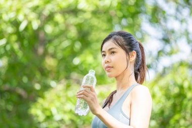 Yeşil Park 'ta plastik şişesi olan genç ve güzel bir sporcu kadın spor yaptıktan sonra su içiyor.