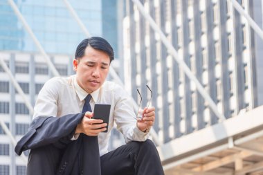 Asyalı işadamı merdivenlerde oturuyor ve ofisin dışındaki cep telefonunda çalışmalarını kontrol ediyor.