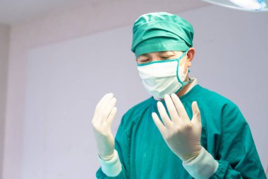 Male surgeon wearing medical protective gloves and surgical mask in operation theater at hospital, Medical team performing surgical operation in operating room
