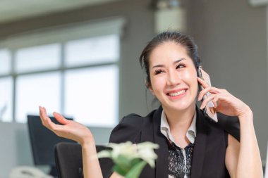 Ofiste çalışan ve telefon kullanan gülümseyen genç bir kadın. Ofiste akıllı telefon kullanan heyecanlı güzel kız.