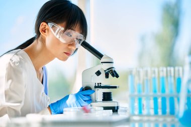 Bilim laboratuarında tıbbi araştırma üzerine çalışan bir bilim adamı mikroskoptan bakıyor.