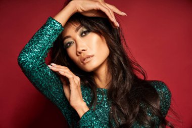 Kırmızı stüdyo arka planında poz veren uzun kıvırcık saçlı güzel Asyalı kadının Vogue tarzı yakın plan portresi. Moda, güzellik konsepti