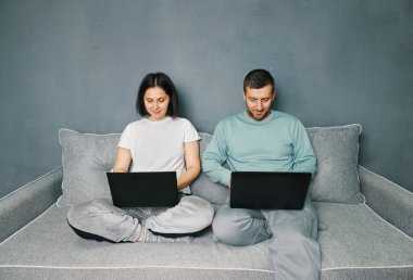 Young couple working on their laptop computer sitting on couch at home. Freelance concept.