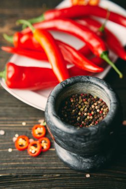 Black marble mortar with a pestle full of mixed peppercorns with red hot chili peppers on background. Spices for cooking, food styling concept