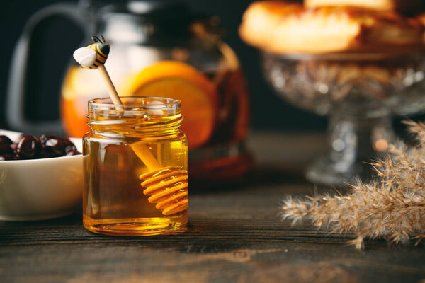 Мед в стеклянной банке с деревянной медовой ковшой на обслуживаемом столе. Органические натуральные ингредиенты, деревенский стиль