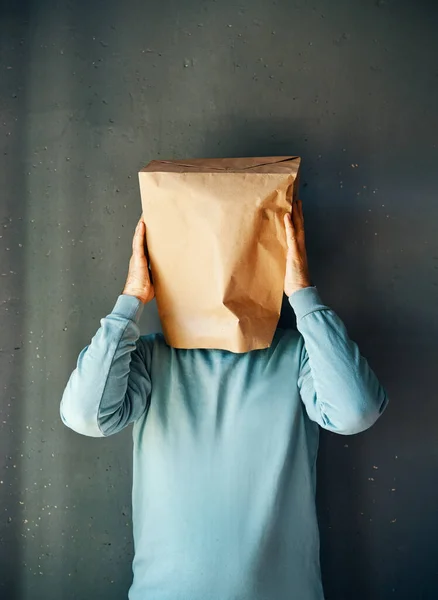 Upset man with a paper bag on head touching temples, suffering from strong tension headache over gray background. Emotion concept