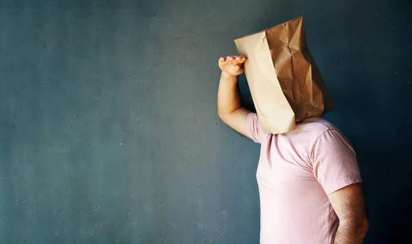 Man with a paper bag on head looking far away distance over gray background with copy space