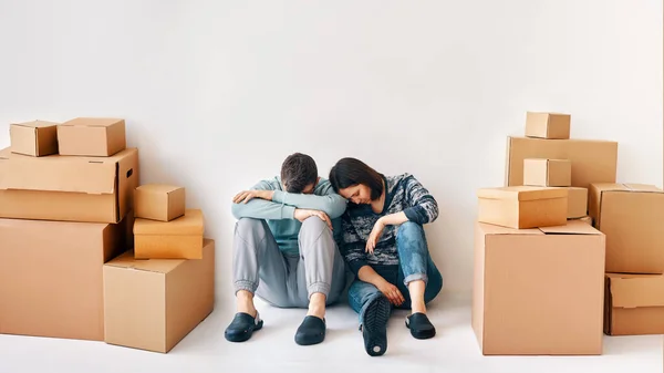 Young couple fell asleep after a moving day sitting on the floor surrounded by cardboard boxes. Tired concept