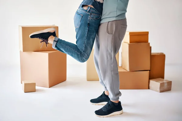Husband lift wife surrounded by cardboard boxes excited to move in new flat, happy couple have fun hugging and celebrating. Relocation concept