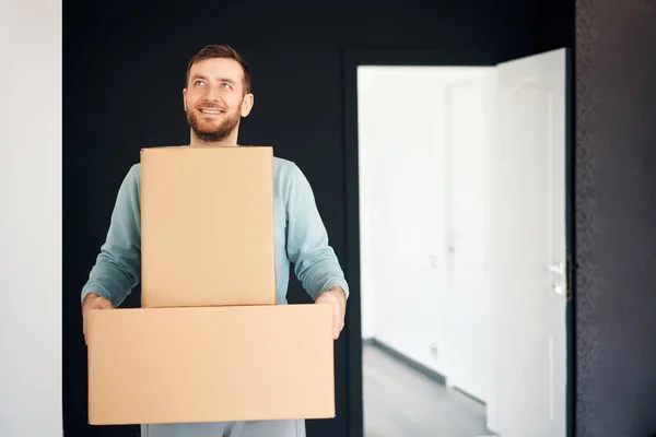 Young smiling man moving into new apartment carrying cardboard boxes. Relocation concept