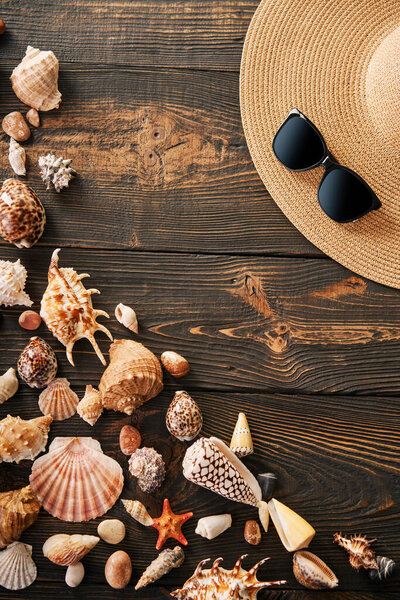 Summer time vacation concept. Straw hat, sunglasses and various seashells on dark wooden background with copy space for text. Flat lay, top view