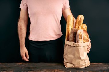 Adam arka planda kağıt torba içinde taze ekmek somunları tutuyor. Fırın, yemek konsepti.