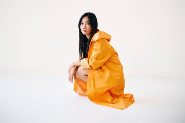 Parlak sarı yağmurluklu güzel Asyalı kız beyaz stüdyo arka planında fotokopi alanı ile poz veriyor.