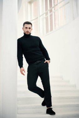 Beyaz merdivenlerde poz veren siyah giysili yakışıklı bir adam modeli. Erkek güzeli.