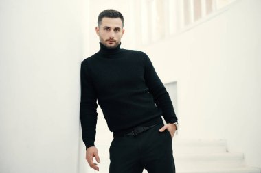 Beyaz merdivenlerde poz veren siyah giysili yakışıklı bir adam modeli. Erkek güzeli.