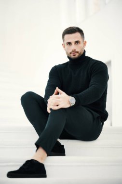 Modaya uygun erkek modeller beyaz merdivenlerde otururlar, siyah kıyafetler giyerler.