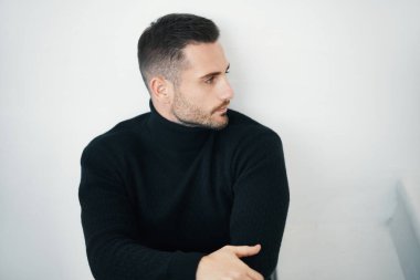 Siyah giysili yakışıklı bir adam beyaz bir arka plana dikkatlice bakıyor..