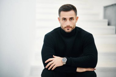 Siyah balıkçı yaka kazak giyen yakışıklı bir gencin, beyaz arka planda kameraya bakarken yakın plan portresi. Uzayı kopyala Erkek güzellik konsepti