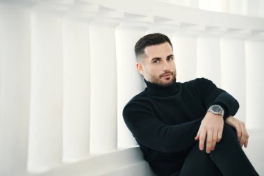 Siyah balıkçı yaka yakalı yakışıklı genç adam. Beyaz arka planda klasik beyaz balyoz ve fotokopi alanı var.