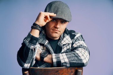 Mavi stüdyo arka planında sandalyede oturan şık ve yakışıklı bir adam. Peaky Blinders stili ilham