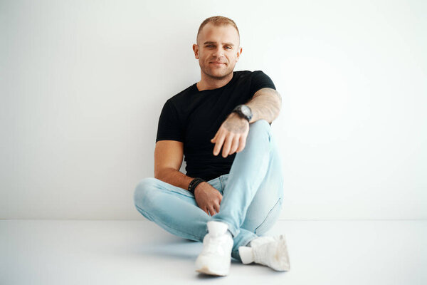 Young handsome man portrait sitting on floor in sun lights with copy space. Male beauty concept
