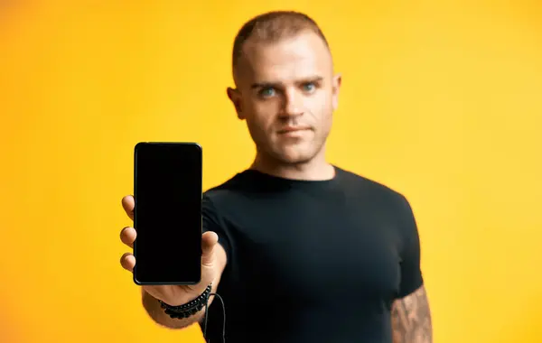 一个自信英俊的男人在黄色背景下拿着空白屏幕手机 图库照片
