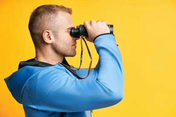 Junger Mann Blickt Durch Ein Fernglas Isoliert Über Gelbem Hintergrund lizenzfreie Stockbilder