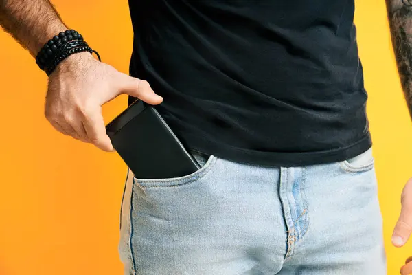便衣人员从口袋里拿出一部黄色背景的手机 免版税图库图片
