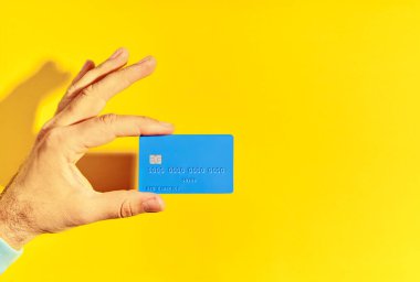 Erkek el mavi plastik banka kartını sarı arkaplanda tutuyor. Para, finans, online alışveriş konsepti