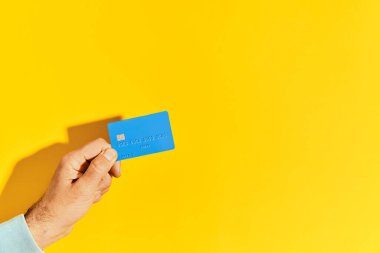 Erkek el mavi plastik banka kartını sarı arkaplanda tutuyor. Para, finans, online alışveriş konsepti