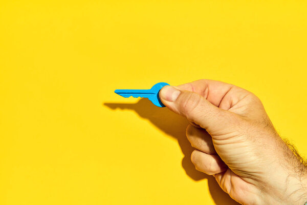 Man Hand Holding Blue Key Bright Yellow Background Copy Space Stock Photo