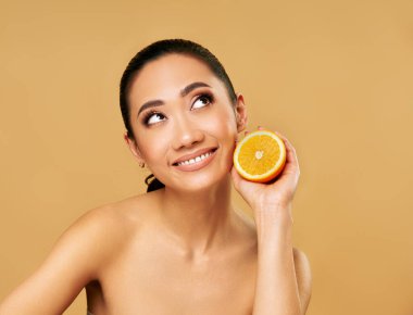 Turunculu güzel Asyalı kadın bej arka planına bakıyor. Güzellik konsepti, cilt bakımı, sağlık ve güzellik.