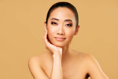 Sağlıklı ciltli, doğal makyajlı ve bej arka planda poz veren güzel bir genç kadın. Güzellik konsepti, cilt bakımı, kişisel bakım konsepti