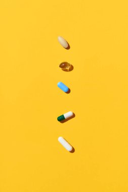 Farklı renklerde çeşitli haplar ve vitaminler ve sarı arka planda fotokopi alanı olan şekiller. Tıp, sağlık hizmeti kavramı